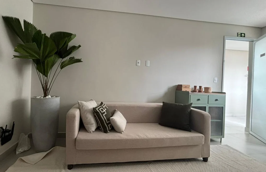 Sala de espera do consultório, com sofá claro, almofadas e planta